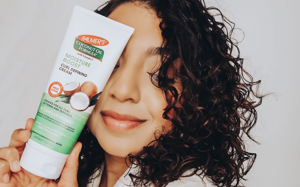 Curly haired woman holding Palmer's Coconut Oil Formula Curl Defining Cream for Heat-Damaged Curls